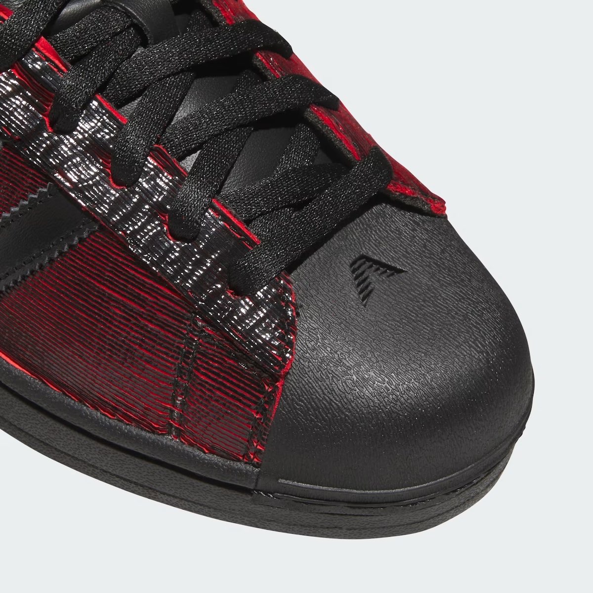 Primer plano de la puntera de la adidas Superstar Halloween de Anthony Edwards, de goma negra lisa con el logo AE y la capellada rayada en negro y rojo
