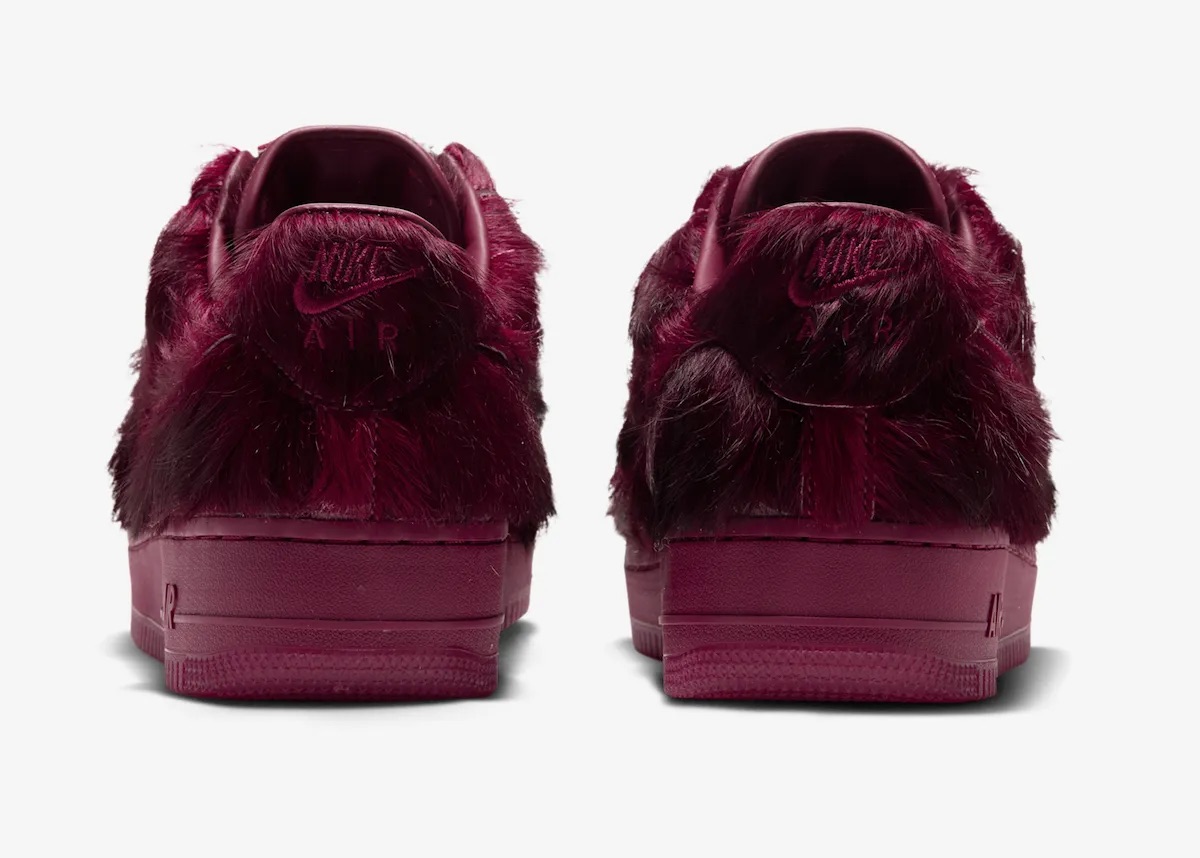 Talones del Nike Air Force 1 Low Pony Hair Team Red sobre fondo gris claro, con el bordado Nike Air medio tapado por el pelo bordó y la suela del mismo color