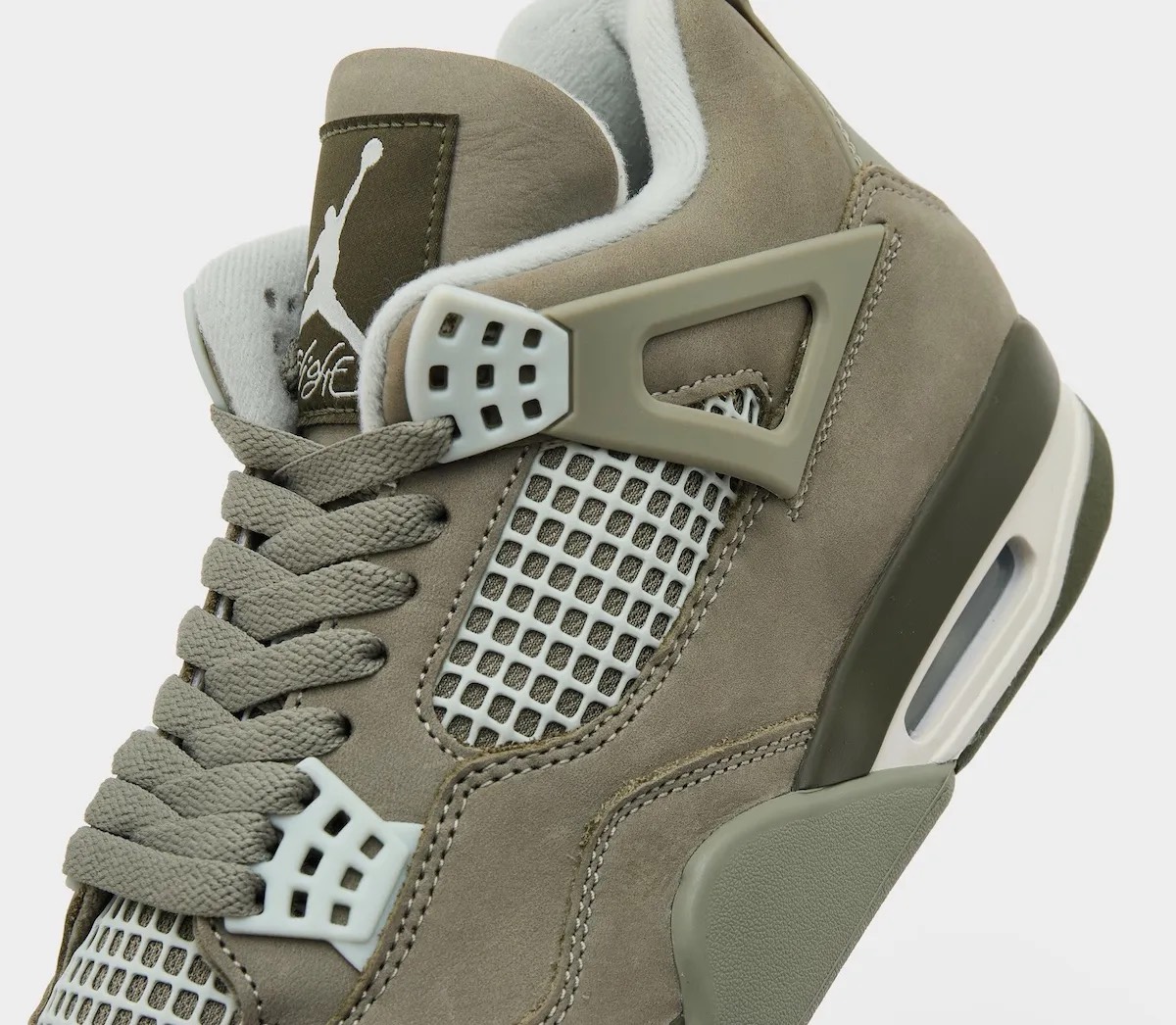 Primer plano del lateral del Air Jordan 4 Light Army, con los cordones verde oliva, el nubuck verde oliva, la malla y los ojales gris claro, el ala lateral del mismo tono que el upper, el parche oscuro de la lengüeta con el Jumpman blanco y la unidad Air visible en el talón