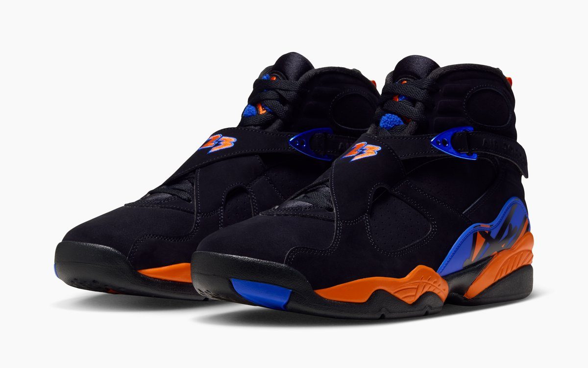 Par de Air Jordan 8 Knicks en negro con entresuela naranja y detalles azules, visto en diagonal sobre fondo blanco