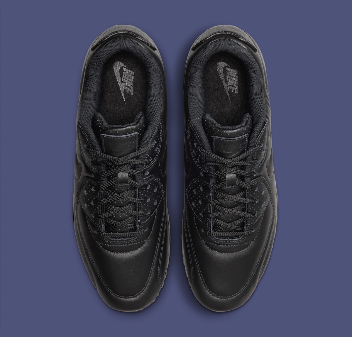 Par de Nike Air Max 90 SP Black Leather vistas desde arriba sobre fondo azul grisáceo, con cuero negro, pasacordones perforados y el logo de Nike en la lengüeta
