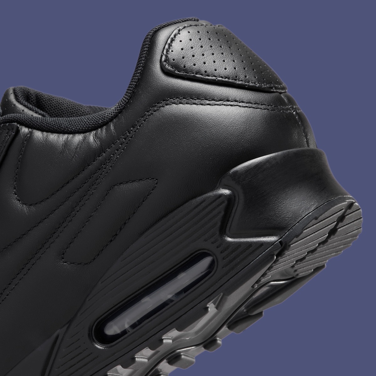 Detalle del talón de la Nike Air Max 90 SP Black Leather sobre fondo azul grisáceo, con cuero negro perforado en la zona del talón y la cámara Air visible en la suela