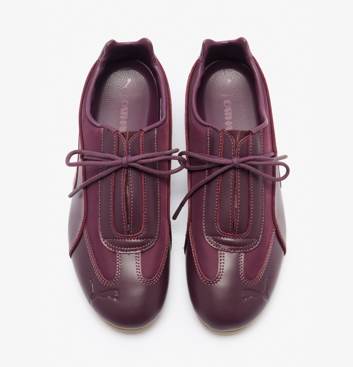Vista superior del par PUMA Speedcat Slip-On de Daniëlle Cathari en cuero bordó, con paneles superpuestos, abertura central en el empeine, cordón fino atado en moño, Cat de PUMA grabado en la punta y la marca Cathari en la plantilla
