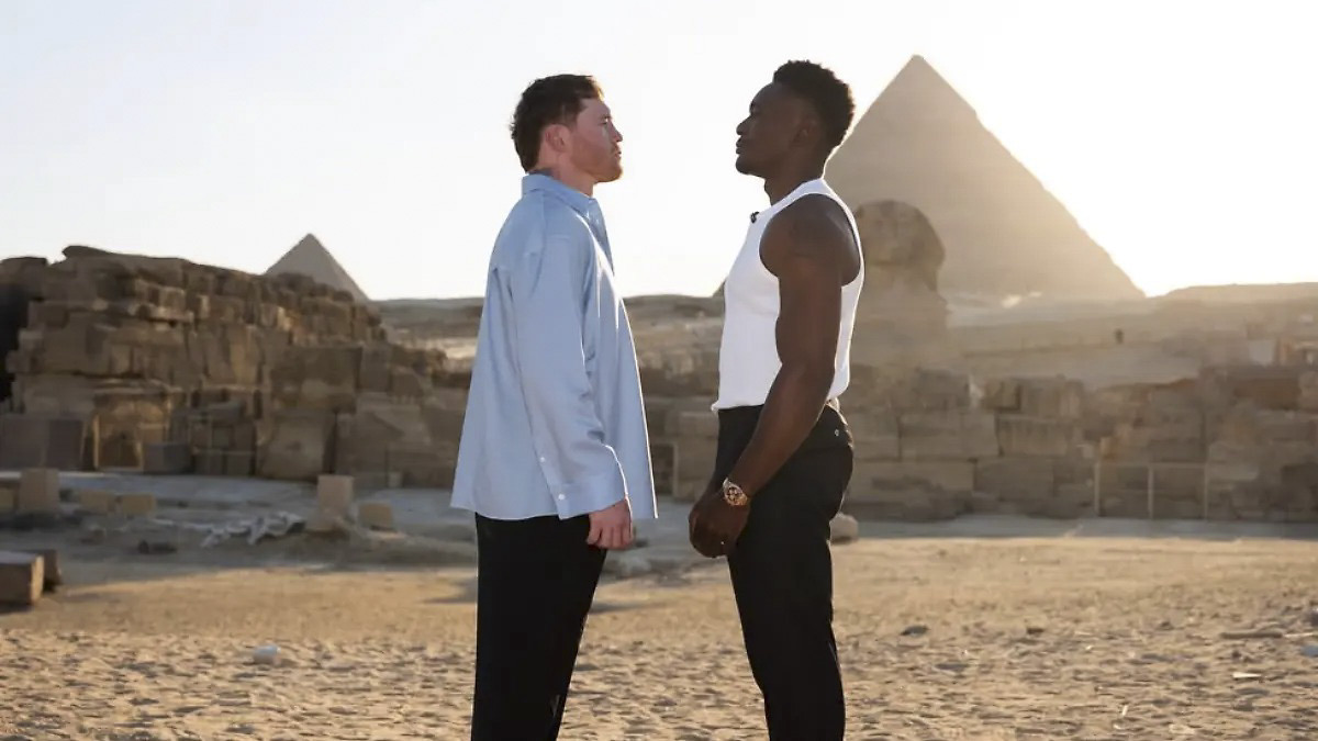 Canelo Álvarez, de camisa celeste, y Christian Mbilli, de musculosa blanca, cara a cara en el desierto con las pirámides de Egipto detrás
