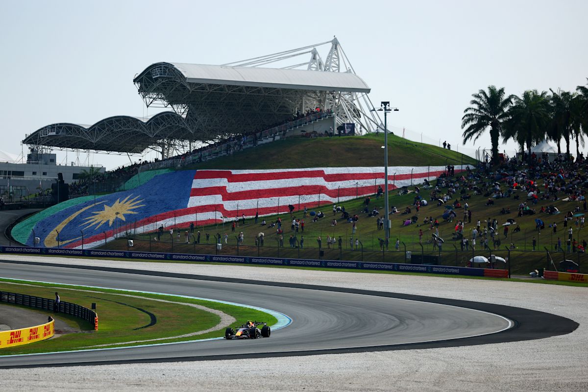 Un Red Bull dobla en Sepang frente a la tribuna principal, con la bandera de Malasia pintada en la colina