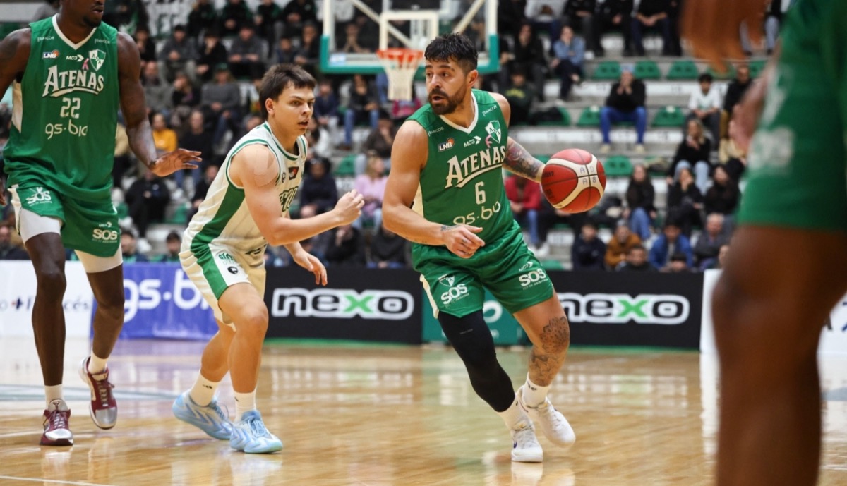 Un jugador de Atenas con la camiseta verde 6 avanza con la pelota ante la marca de un jugador de Ferro con camiseta blanca y verde, en la cancha de Atenas en Córdoba