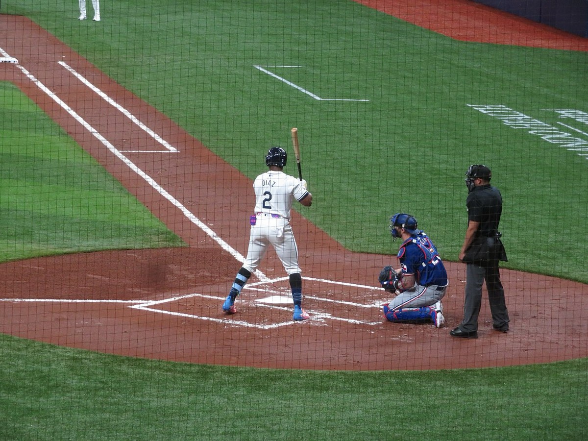 Foto de archivo: Yandy Díaz, de los Tampa Bay Rays, con la camiseta blanca número 2, espera el lanzamiento en el plato de Tropicana Field, con el receptor de los Texas Rangers agachado y el umpire detrás, vistos a través de la red