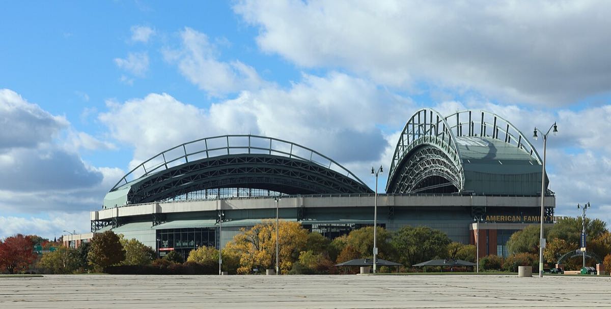 Imagen del estadio: el American Family Field de Milwaukee, con su techo de arcos metálicos, rodeado de árboles con colores de otoño