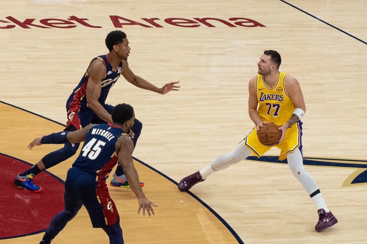Foto de archivo: Luka Doncic, con la camiseta amarilla número 77 de los Lakers, sostiene la pelota frente a dos jugadores de los Cleveland Cavaliers, de azul