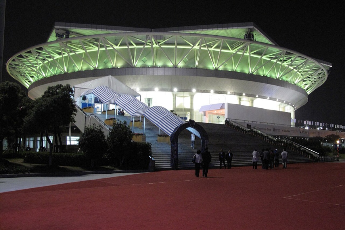 Foto de archivo: el Qi Zhong Stadium de Shanghái de noche, con el techo iluminado de verde y la escalinata de entrada, con gente caminando adelante