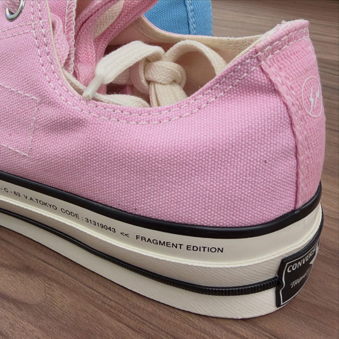 Detalle lateral de la Converse Chuck Taylor baja de fragment design rosa, con el rayo de fragment en el talón y la inscripción V.A.TOKYO y FRAGMENT EDITION en la entresuela
