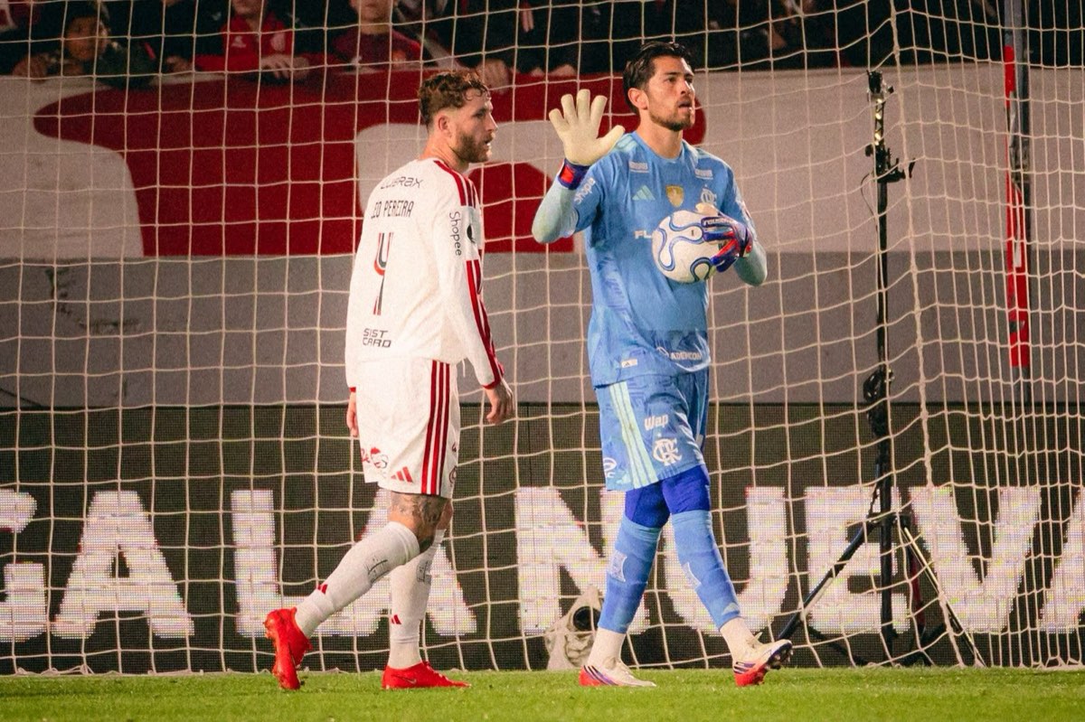 Agustín Rossi, arquero de Flamengo, con buzo celeste y la pelota en la mano izquierda, levanta la otra mano junto a Léo Pereira, de camiseta blanca con el número 4, frente al arco del estadio UNO durante la ida de la semifinal (foto: Adriano Fontes / prensa oficial de Flamengo, CRF)