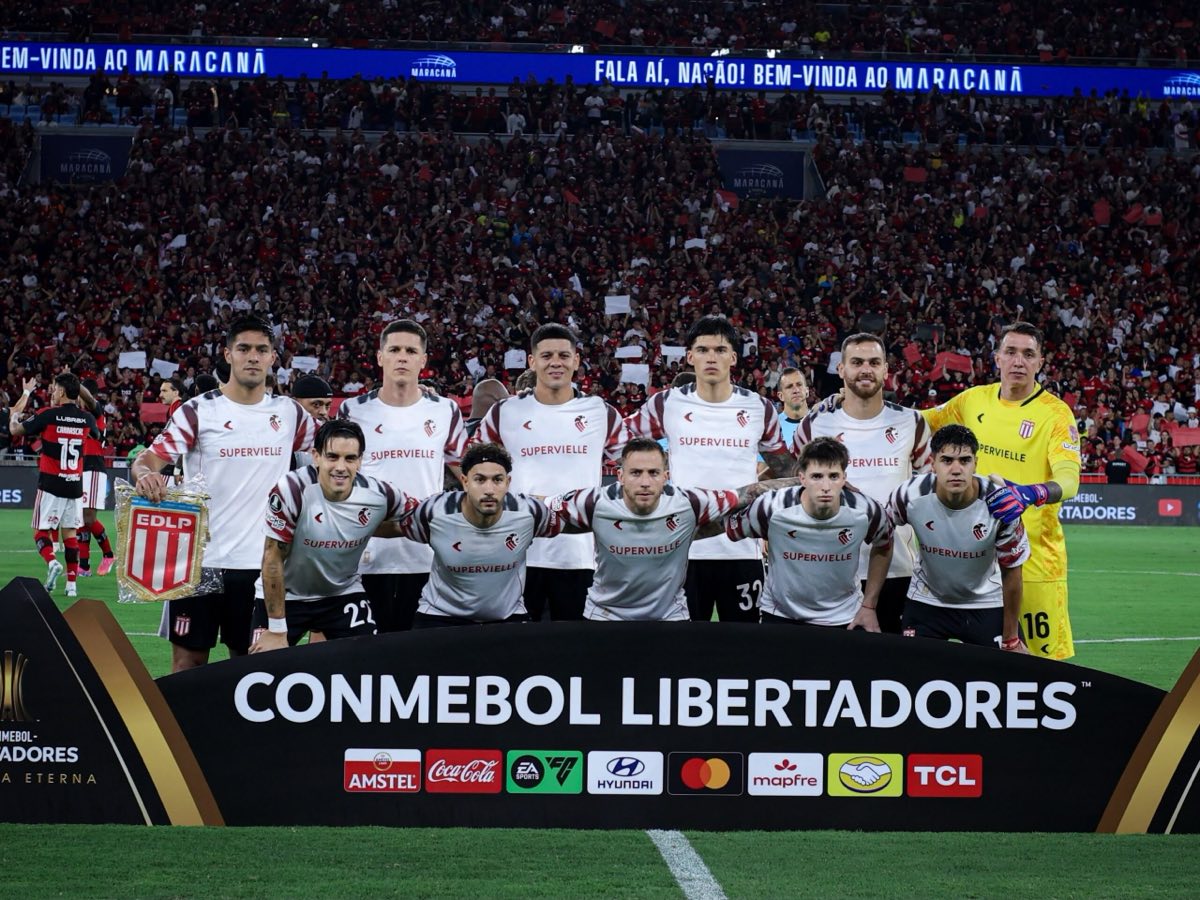 El equipo titular de Estudiantes, con la camiseta blanca con detalles rojos, posa para la foto antes de la vuelta de la semifinal en el Maracaná, con la tribuna de Flamengo llena de fondo (foto: prensa Estudiantes de La Plata)