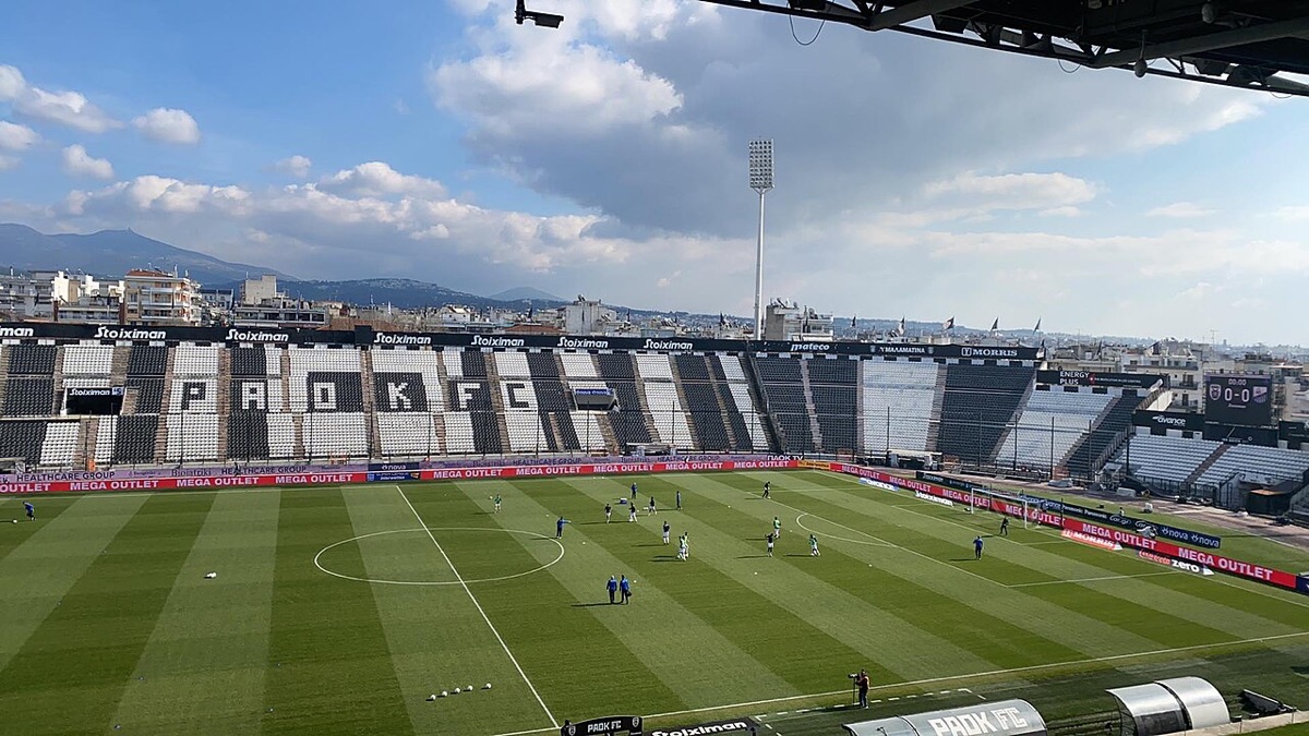 Vista del Toumba de Salónica, el estadio del PAOK, con las tribunas vacías y los jugadores haciendo la entrada en calor (foto de archivo: Αθλητικά, Wikimedia Commons, CC BY-SA 4.0)