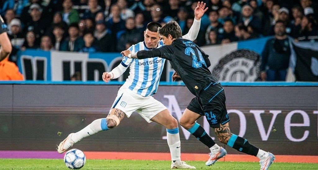 Un jugador de Racing, con la camiseta albiceleste, protege la pelota ante la marca de un futbolista de Belgrano con la camiseta negra número 24 en el Cilindro de Avellaneda (foto: prensa Racing Club)