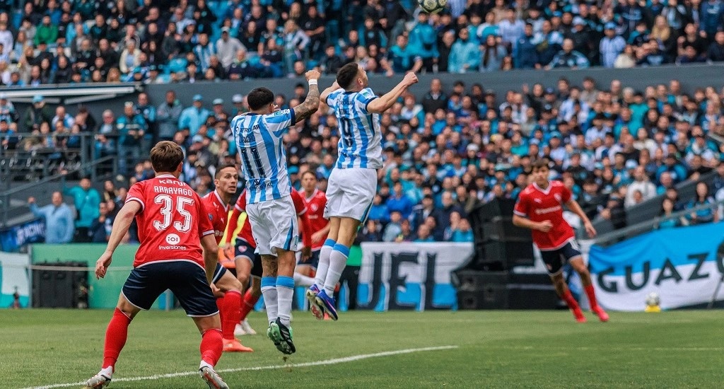 Jugadores de Racing, de celeste y blanco, saltan a cabecear dentro del área de Independiente, mientras un defensor del Rojo con el número 35 mira la jugada, con las tribunas llenas del Cilindro de fondo (foto: prensa Racing Club)