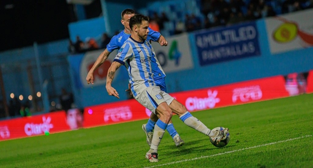 Un jugador de Racing, con la camiseta albiceleste, juega la pelota ante la marca de un rival de Estudiantes de Río Cuarto en el estadio Antonio Candini (foto: Racing Club)