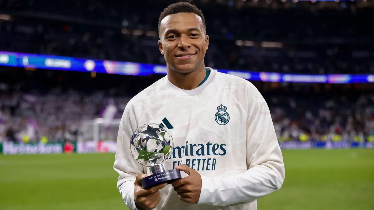 Kylian Mbappé, con buzo blanco del Real Madrid, sonríe con el trofeo de jugador del partido en la mano en el césped del Bernabéu (foto: Real Madrid)