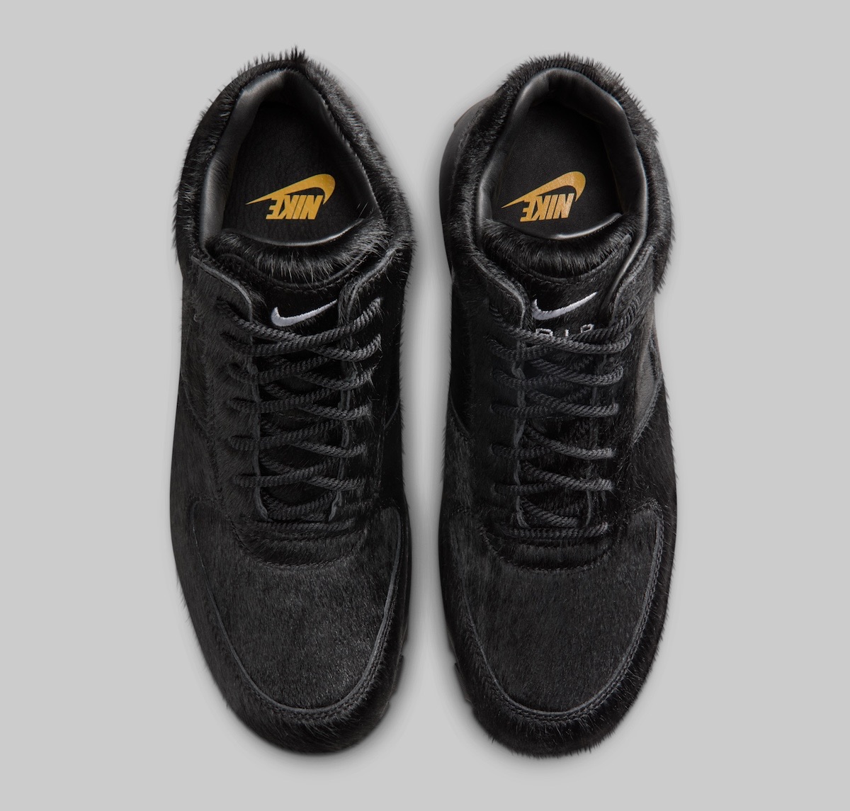 Par de Nike Air Max Goadome Black Pony Hair visto desde arriba sobre fondo gris, con la plantilla negra y el logo de Nike en dorado