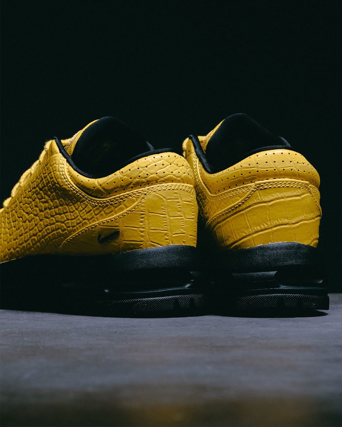 Vista trasera del par del Nike Air Max Goadome Low Yellow Croc, con el talón de cuero amarillo grabado tipo cocodrilo, perforaciones en el cuello, borde negro en la boca de la zapatilla y base negra con la unidad Air a la vista
