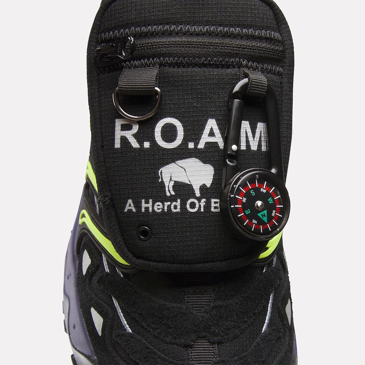 Primer plano del bolsillo de la Reebok DMX Trailzillo de A Herd of Bison, negro con la inscripción R.O.A.M, el bisonte y una brújula colgada de un mosquetón