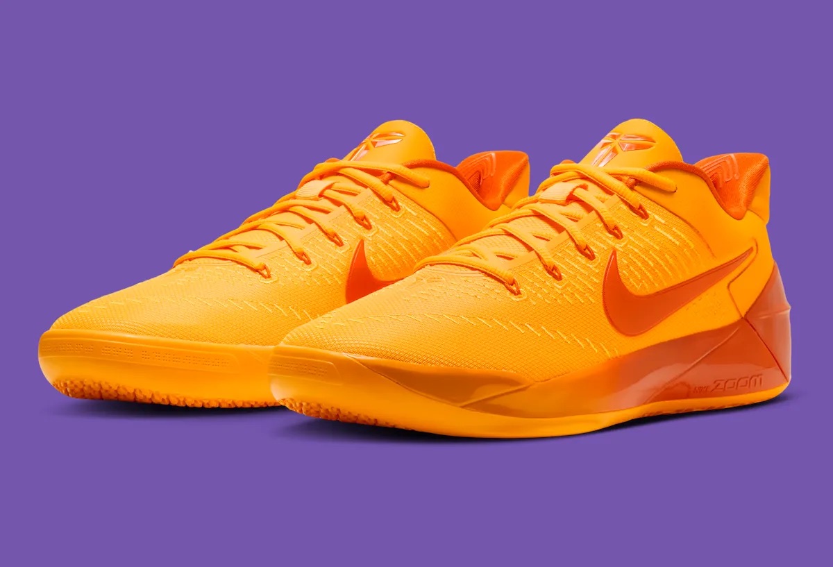 Nike Kobe AD Protro en Laser Orange de perfil sobre fondo violeta, con upper naranja claro, swoosh grande naranja oscuro, mediasuela naranja rojiza con la palabra Zoom y suela naranja