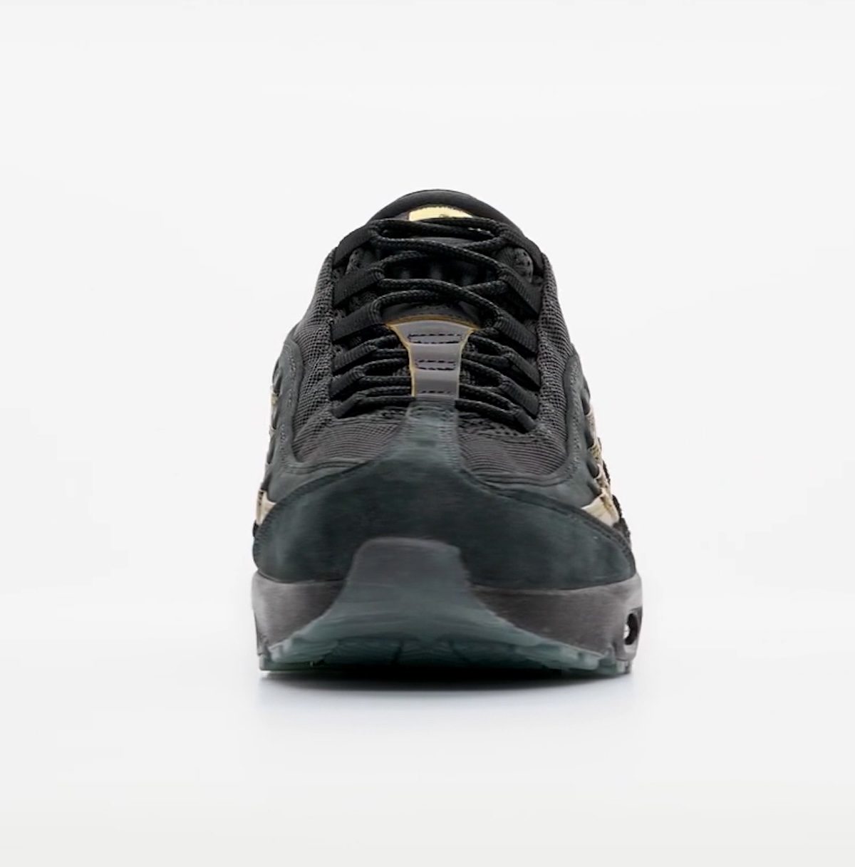 Kyle Wilson x Nike SB Air Max 95 visto de frente sobre fondo gris claro, con la puntera de gamuza negra, los cordones negros y los paneles con brillo dorado