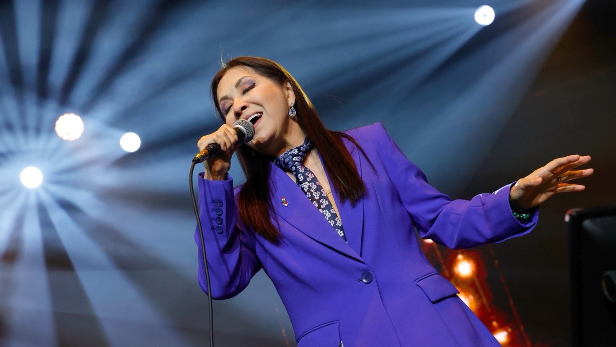 Foto de prensa de Ana Gabriel cantando en vivo con saco violeta, bajo luces azules