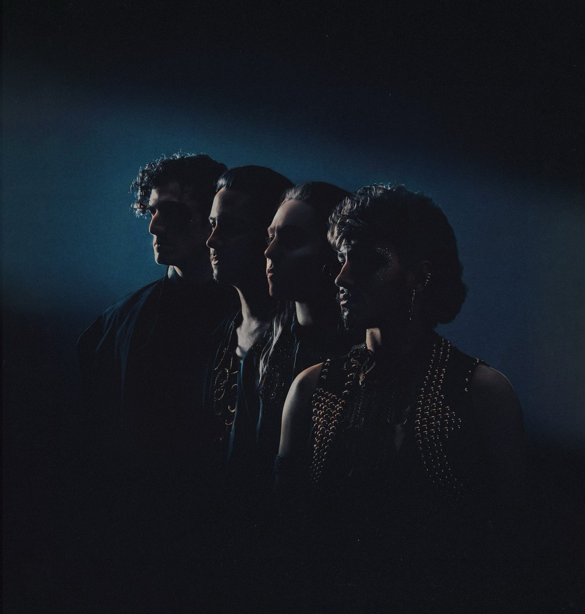 Los cuatro integrantes de Greta Van Fleet de perfil, en fila y casi en silueta, iluminados por una luz azul sobre fondo negro