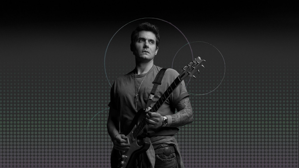 Foto oficial de la residencia de John Mayer en la Sphere: el músico, en blanco y negro, con remera, collar largo y una guitarra eléctrica, mirando hacia un costado sobre un fondo oscuro de puntos y círculos