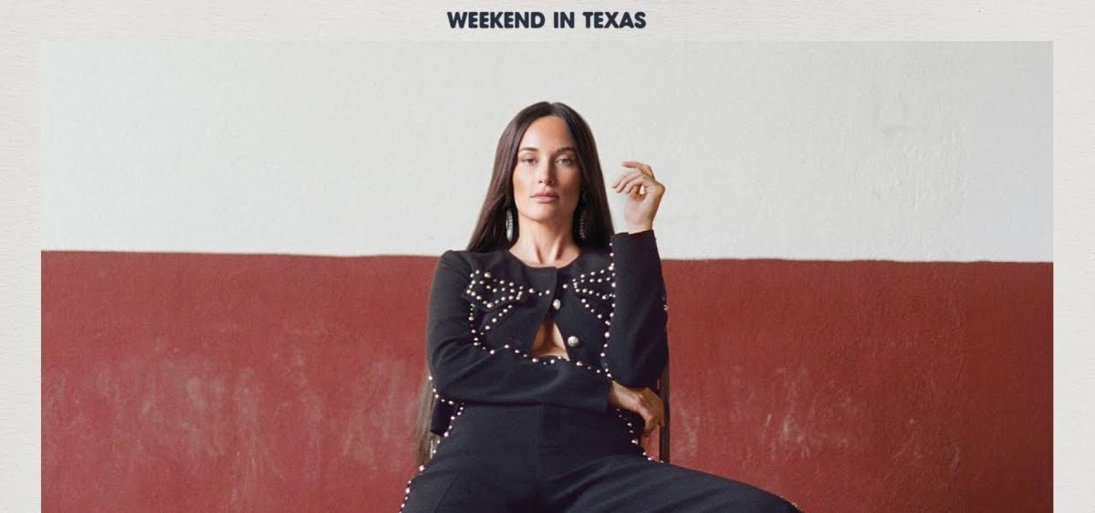 Arte oficial de «Weekend in Texas»: Kacey Musgraves, con pelo largo oscuro y un conjunto negro con apliques de perlas y un moño, sentada en una silla frente a una pared blanca y bordó