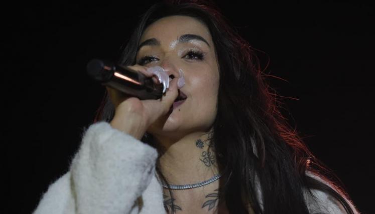 María Becerra cantando con micrófono en mano y un abrigo blanco de piel, durante una presentación de
