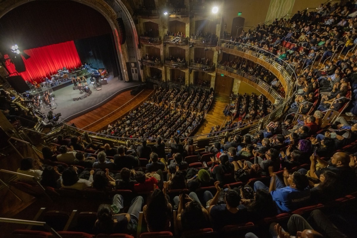 Vista desde los palcos superiores de la Sala Principal del Palacio de Bellas Artes llena de público, con el escenario a la izquierda, el telón rojo y los instrumentos de la orquesta. Foto: Secretaría de Cultura