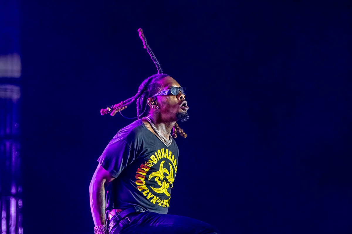 Foto de archivo de Offset en el escenario del Clout Festival 2024, con anteojos oscuros, trenzas en el aire y una remera negra con estampa amarilla, bajo luces violetas