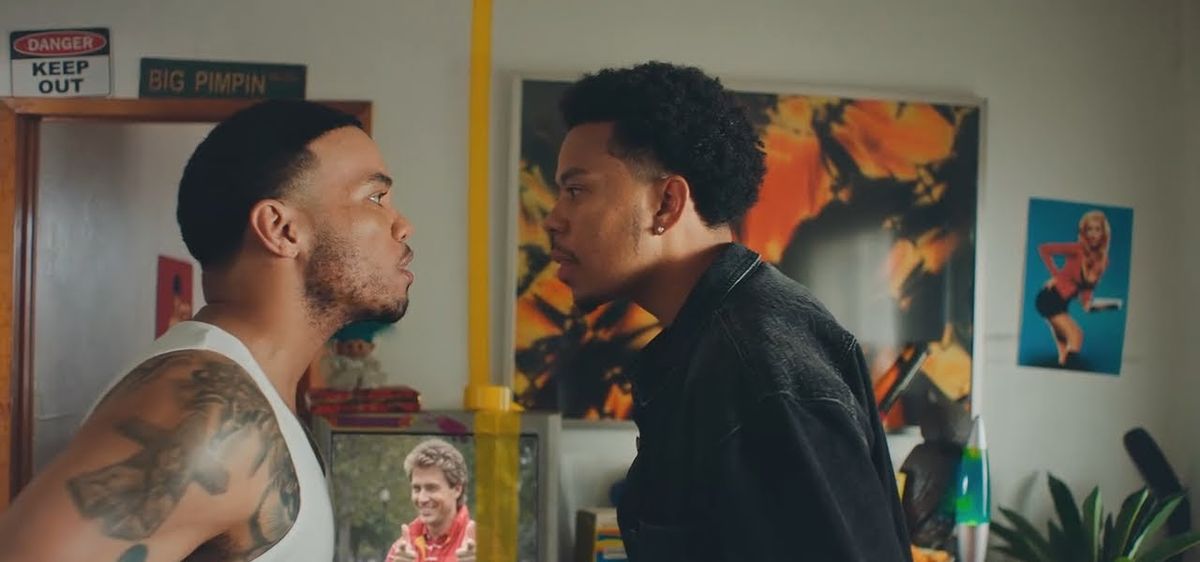 Fotograma de archivo del video oficial de «A Good Day»: el dúo cara a cara, uno con musculosa blanca y el otro con camisa negra, en un living lleno de cuadros y pósters