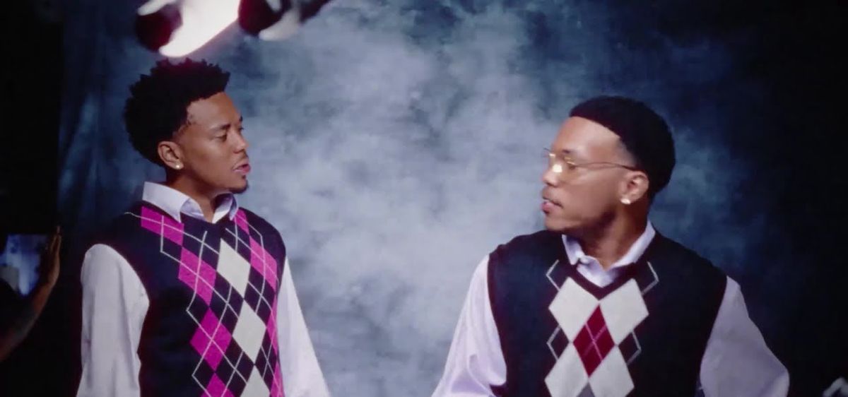 Fotograma del visualizer oficial de «Days Go By»: Cordae y Anderson .Paak, con chalecos de rombos rosa y bordó sobre camisas claras, se miran de reojo frente a un fondo de humo azul