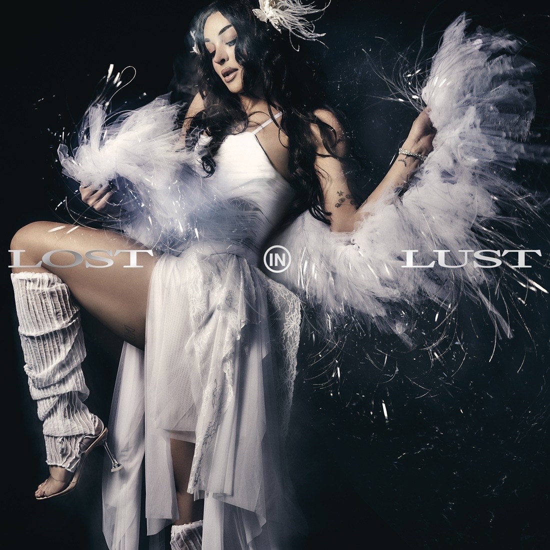 Portada de Lost in Lust de Pabllo Vittar: la artista con vestido blanco, polainas de tejido y una estola de plumas y fibras brillantes sobre fondo negro, con el título en letras plateadas