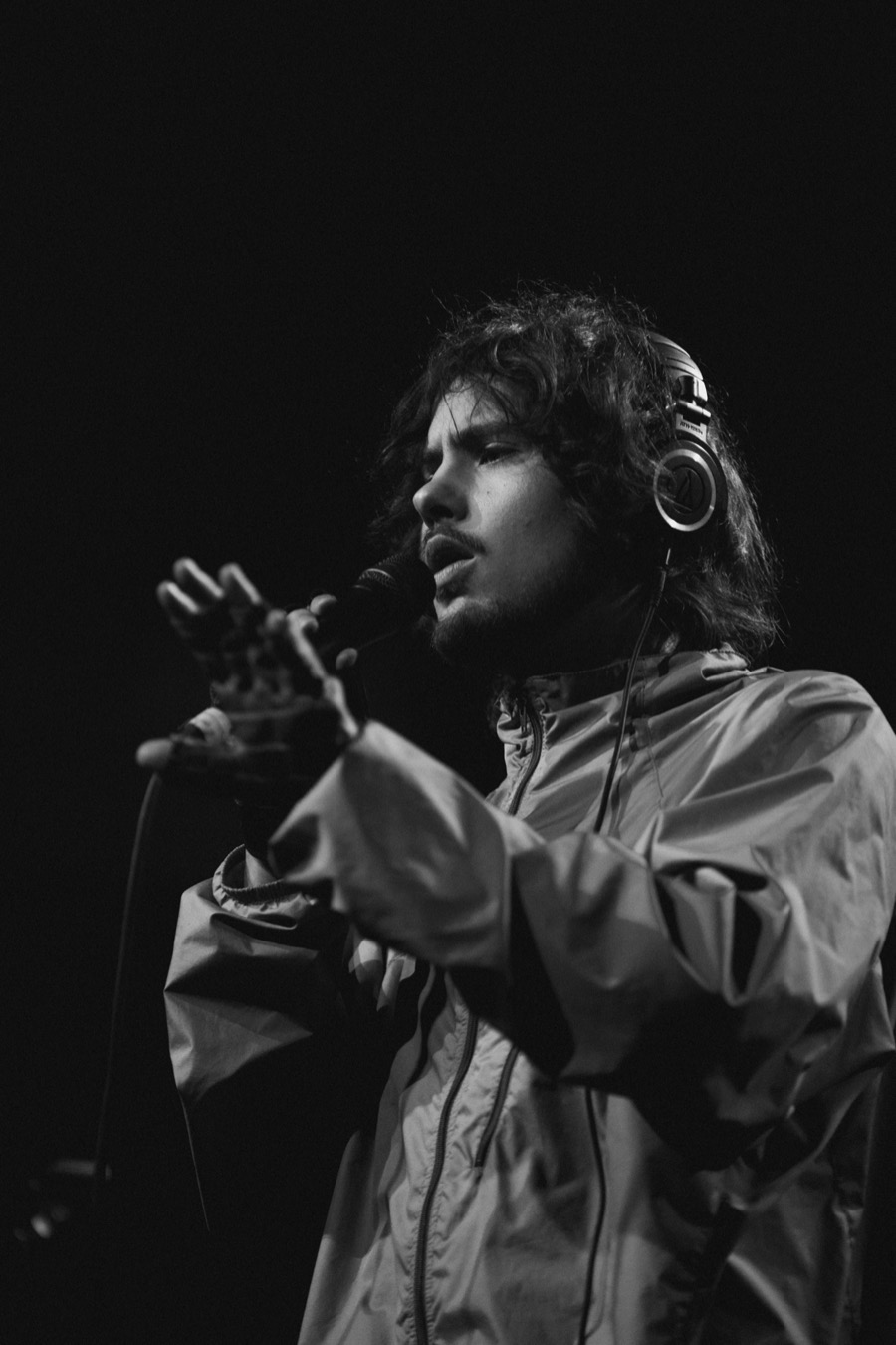 Foto de archivo en blanco y negro de Quadeca en vivo durante su gira de 2024, con auriculares, campera rompevientos y el micrófono en la mano, extendiendo la otra mano hacia el público