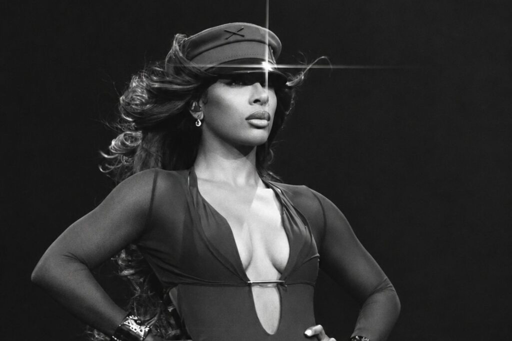 Victoria Monét en blanco y negro sobre fondo oscuro, con gorra, body escotado y las manos en la cintura