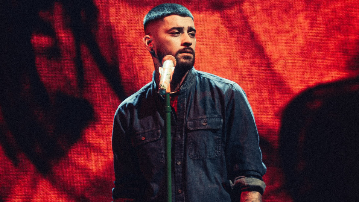 ZAYN cantando en vivo frente a un micrófono de pie, con camisa de jean, delante de una pantalla gigante con visuales en rojo, durante el show del 2 de octubre en Santiago de Chile. Foto: DG Medios / Andie Borie