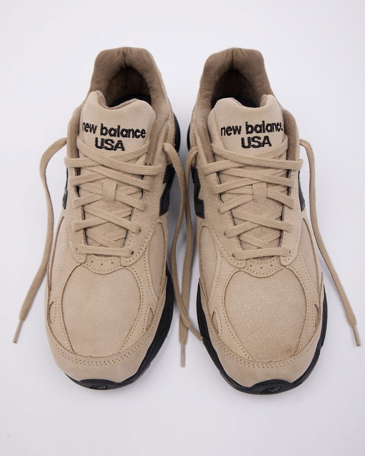 Par del JJJJound x New Balance 990v3 Tan Suede de frente, con cordones tan, lengüetas con la leyenda new balance USA bordada en negro y suela negra