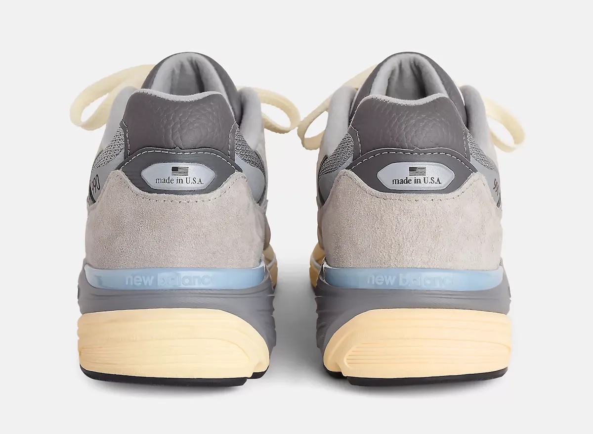 Talones del New Balance 990v7 Made in USA Kool Grey sobre fondo gris claro, con la gamuza gris, la etiqueta Made in USA y la entresuela con una franja celeste y la base amarilla