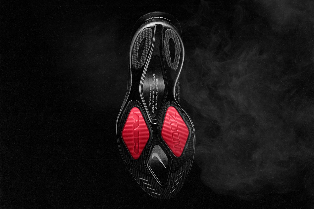 Suela de la Nike Apex negra vista desde abajo, con dos rombos de goma roja que dicen AIR y ZOOM bajo el antepié, un Swoosh en el medio y la inscripción Nike Apex Racing System en el arco
