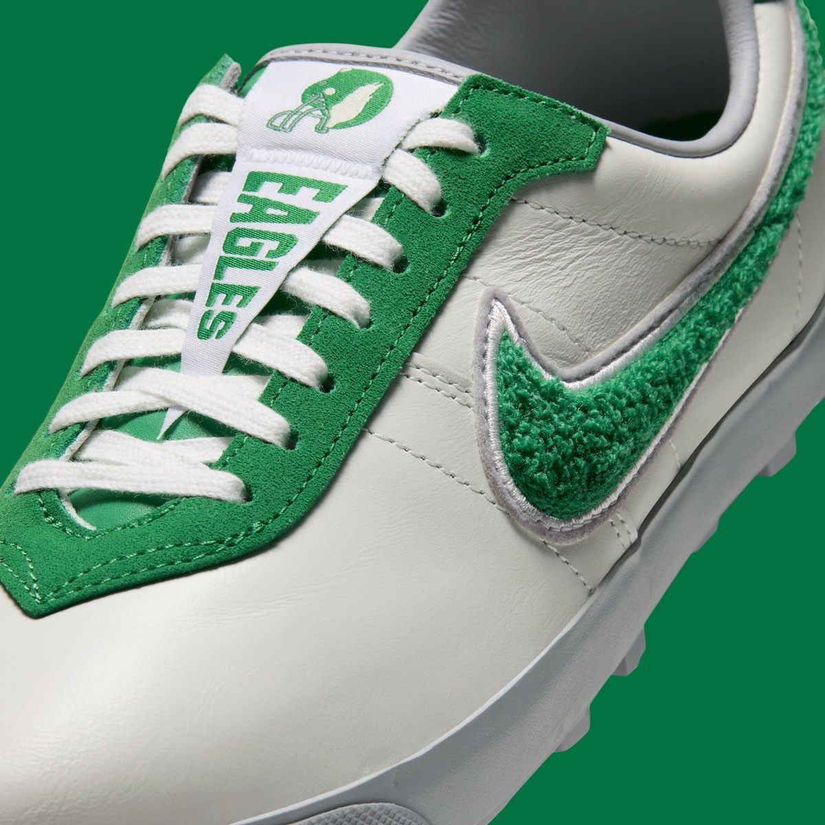Detalle del Nike Astro Grabber de los Philadelphia Eagles con upper de cuero blanco, Swoosh de chenille verde y banderín de Eagles en la lengüeta