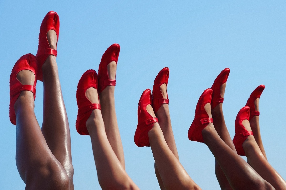 Piernas de porristas en el aire contra un cielo celeste, todas con la NikeSKIMS Rift Satin University Red, en una foto de la campaña de The Varsity Collection