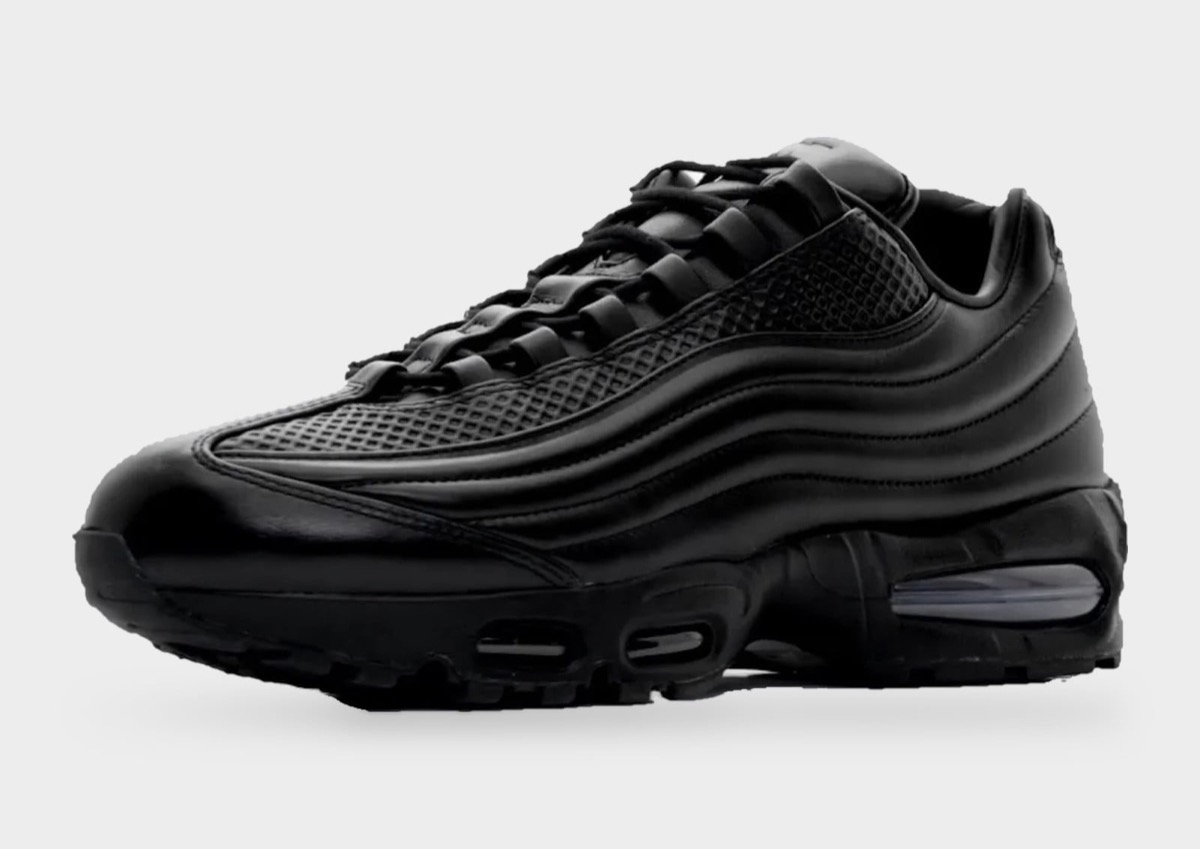 Nike Air Max 95 Lux de One Block Down de perfil sobre fondo gris claro, toda de cuero negro con las capas onduladas del lateral, cordones negros y la cámara Air azulada en el talón