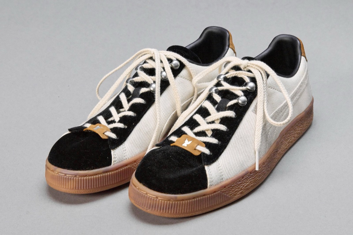 Par de PUMA x MASU Curio Suede Ivory x Black sobre fondo gris, con cuerpo marfil, puntera y zona de cordones en gamuza negra, ganchos plateados, cordones crudos, etiqueta marrón en los cordones y suela de goma color caramelo