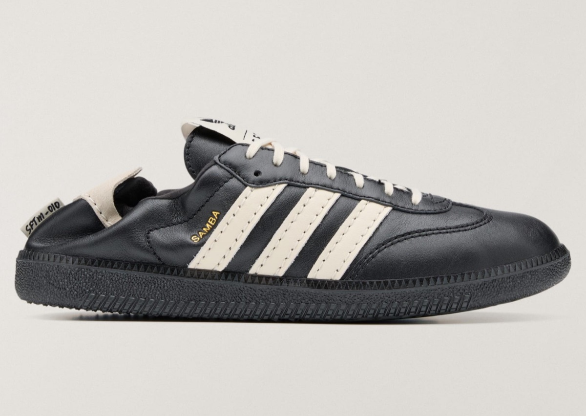Vista lateral del adidas Samba OG de Song for the Mute en cuero negro con las tres tiras en cuero crema, la palabra Samba en dorado, cordones crema, suela negra y el talón hundido hacia adentro con una etiqueta que dice SFTM-010, sobre fondo gris claro