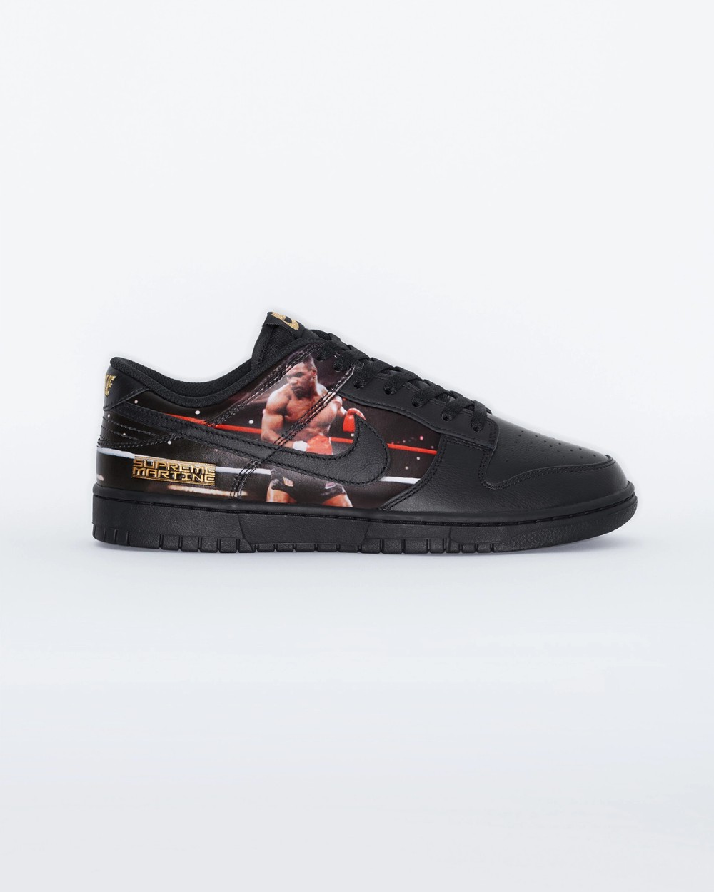 Vista lateral del Supreme x Martine Rose x Nike Dunk Low Tyson sobre fondo blanco, en cuero negro con suela negra, la foto de Mike Tyson con guantes rojos en el ring detrás del swoosh negro y la placa dorada Supreme Martine cerca del talón