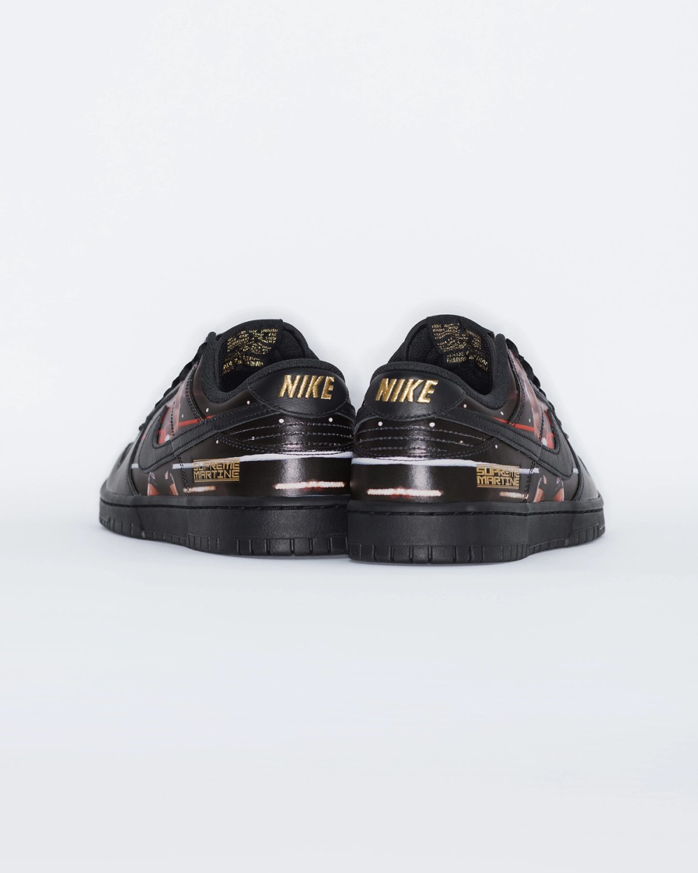 Vista trasera del par del Supreme x Martine Rose x Nike Dunk Low Tyson sobre fondo blanco, con la palabra Nike en dorado en cada talón, la placa dorada Supreme Martine y parte de la foto del ring en negro, rojo y blanco